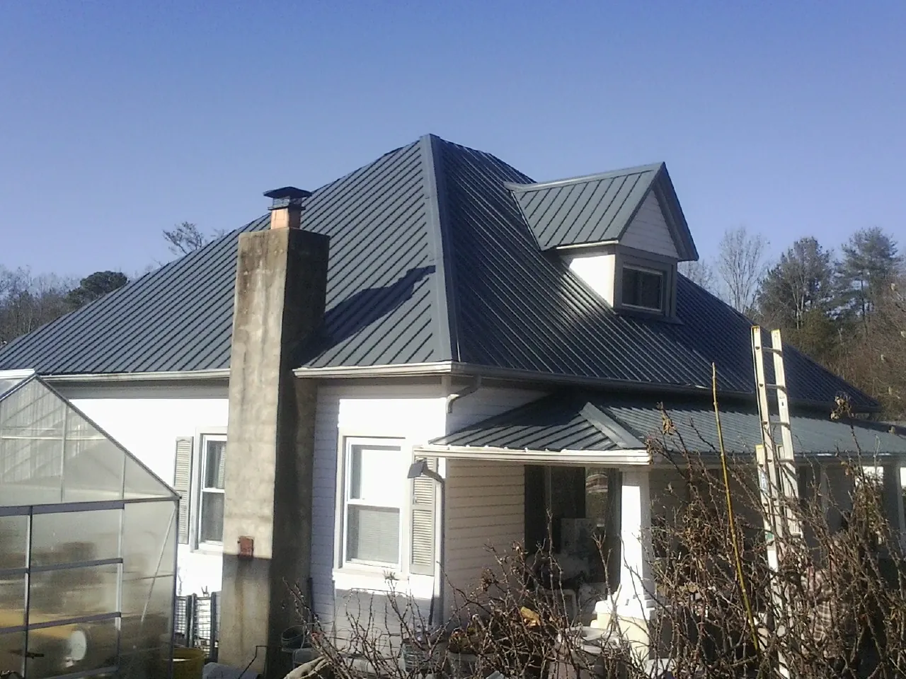 Dark blue standing seam metal roof on a white farmhouse with dormer — Slate & Tile Roof Repair by Roofing Brothers in Mount Olivet