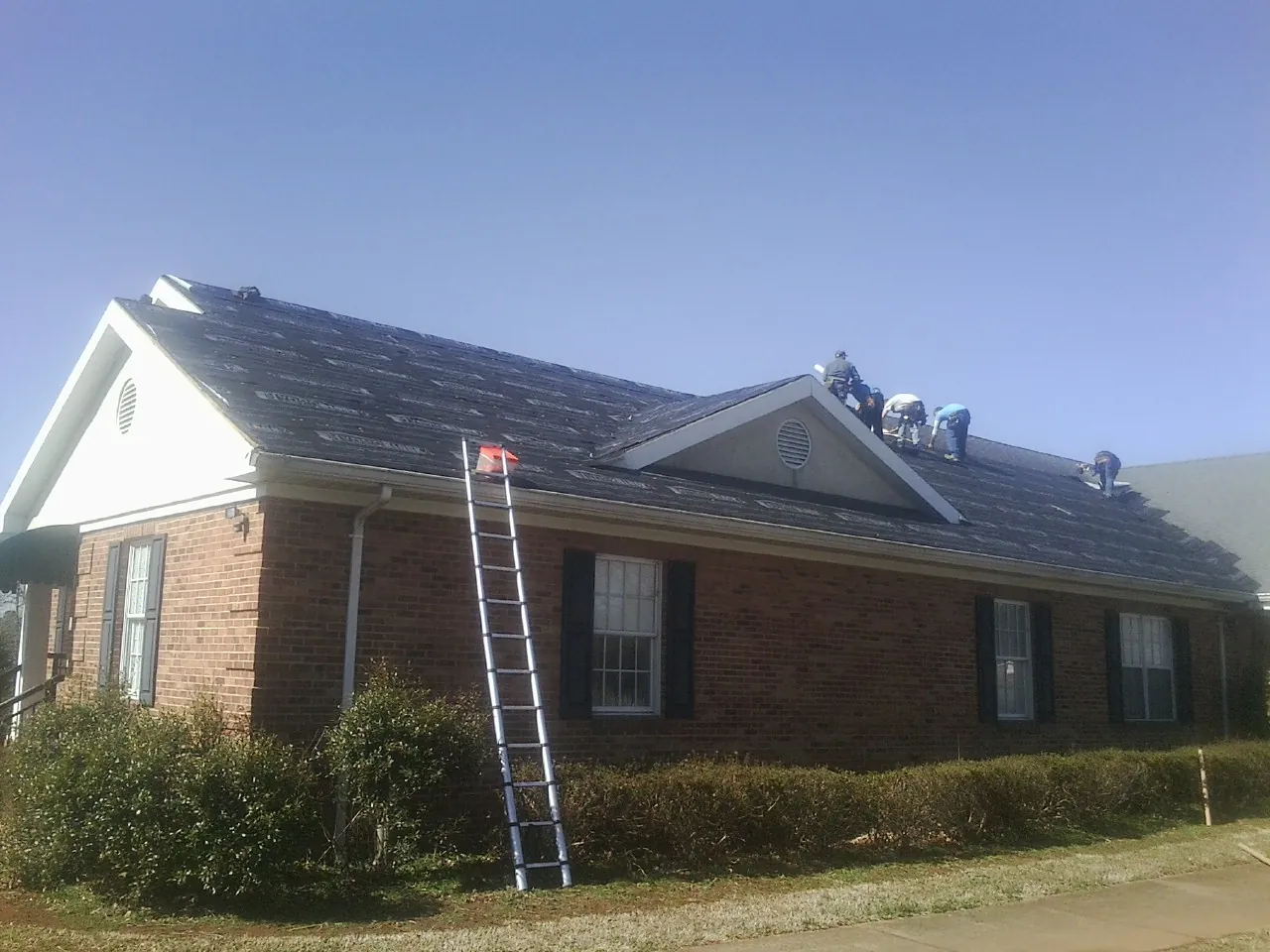 Crew tearing shingles off a brick ranch roof with a ladder set — Metal Roof Repair work by our crew in Mount Olivet