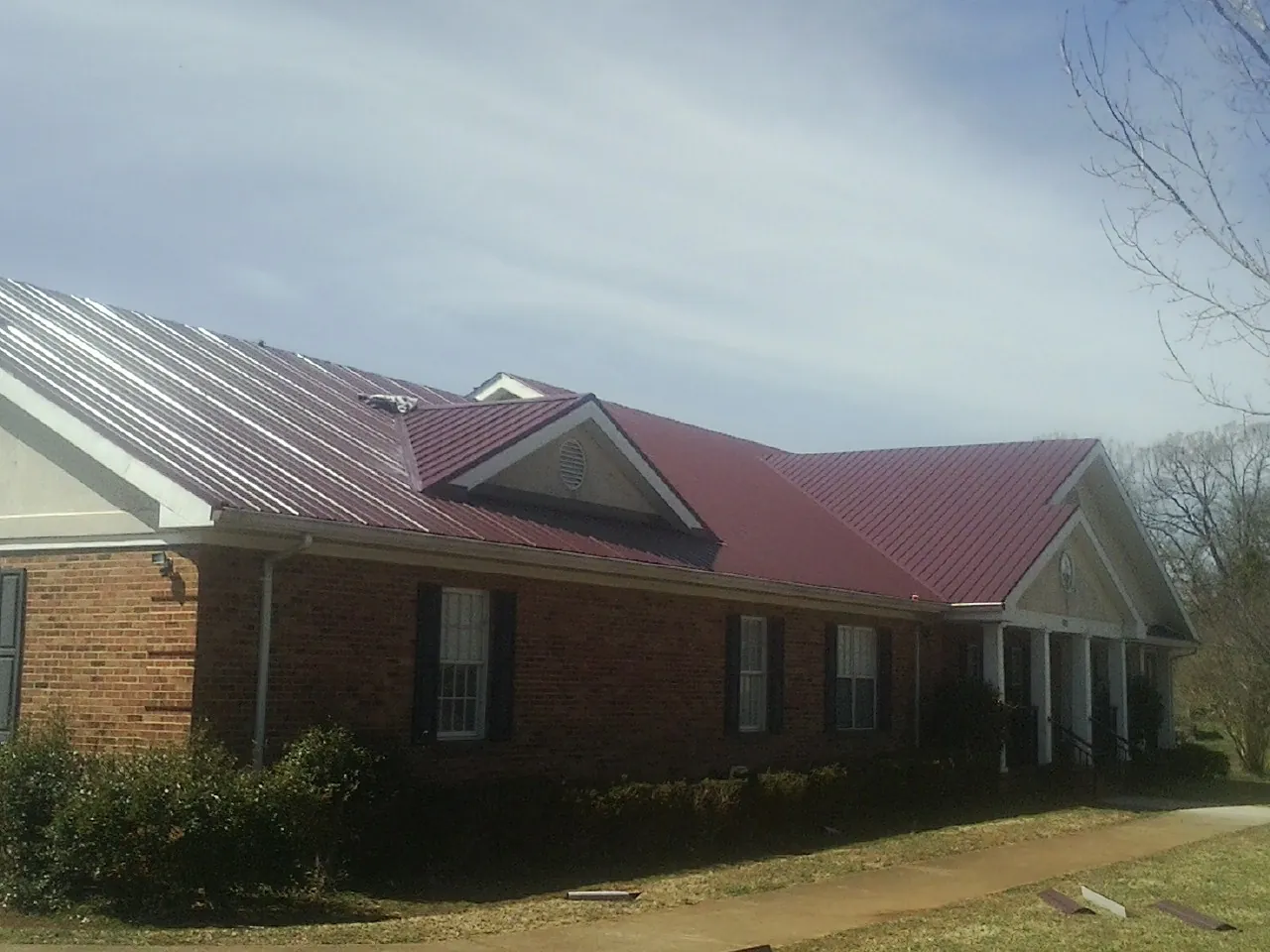 Red metal roof with gabled entries on a long brick building, from a Hail Damage Roof Repair job in Mount Olivet