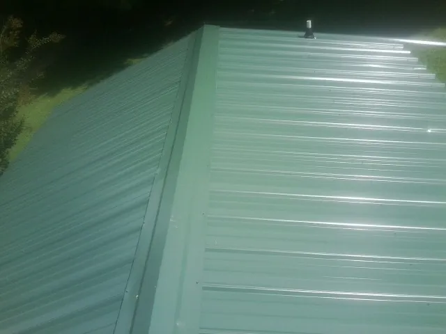 New green metal panels meeting at the ridge of a roof — Flat Roof Repair work by our crew in Mount Olivet