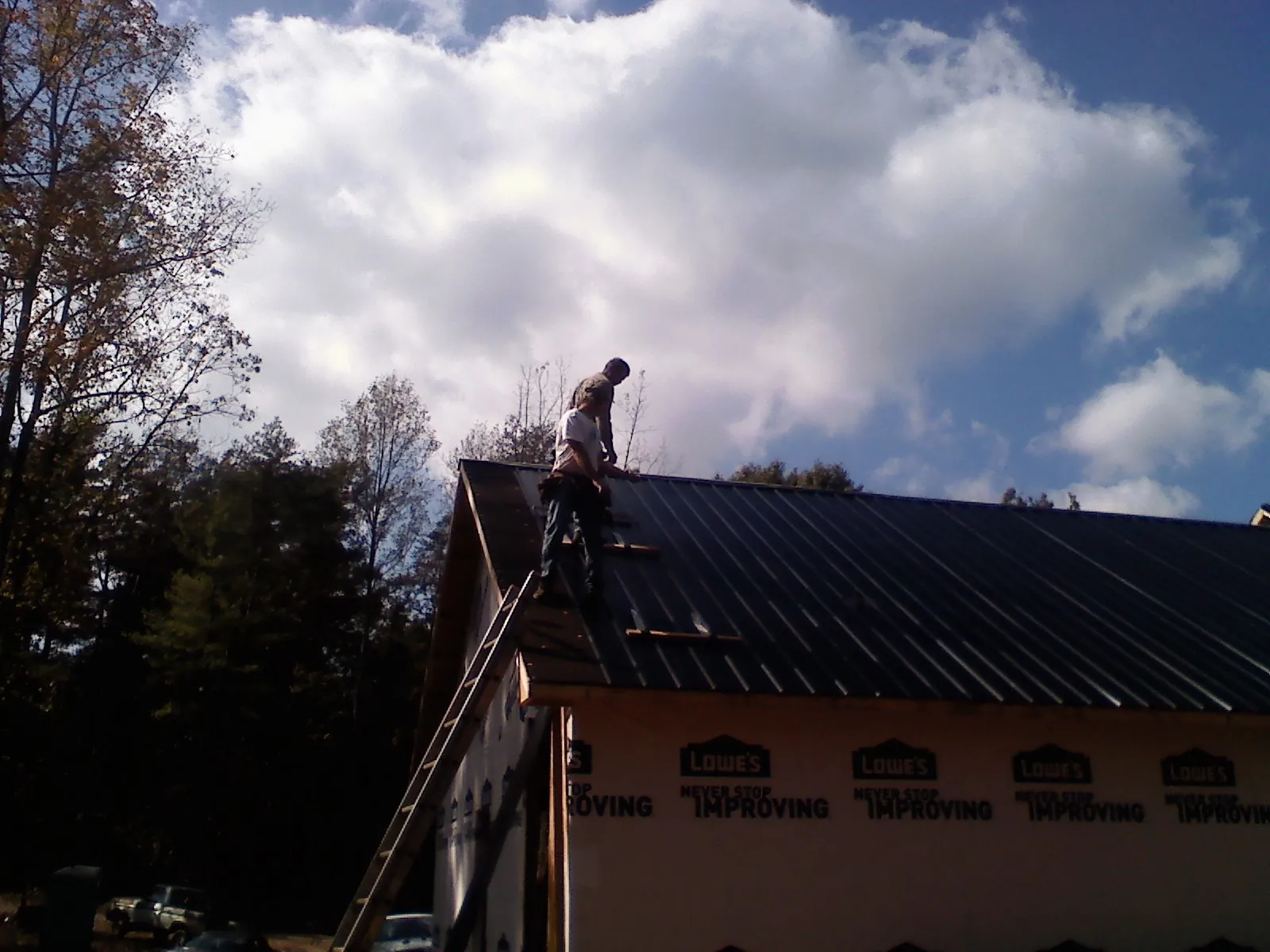 Roofer fastening dark metal panels high against a cloudy sky, from a Roof Inspection job in Mount Olivet