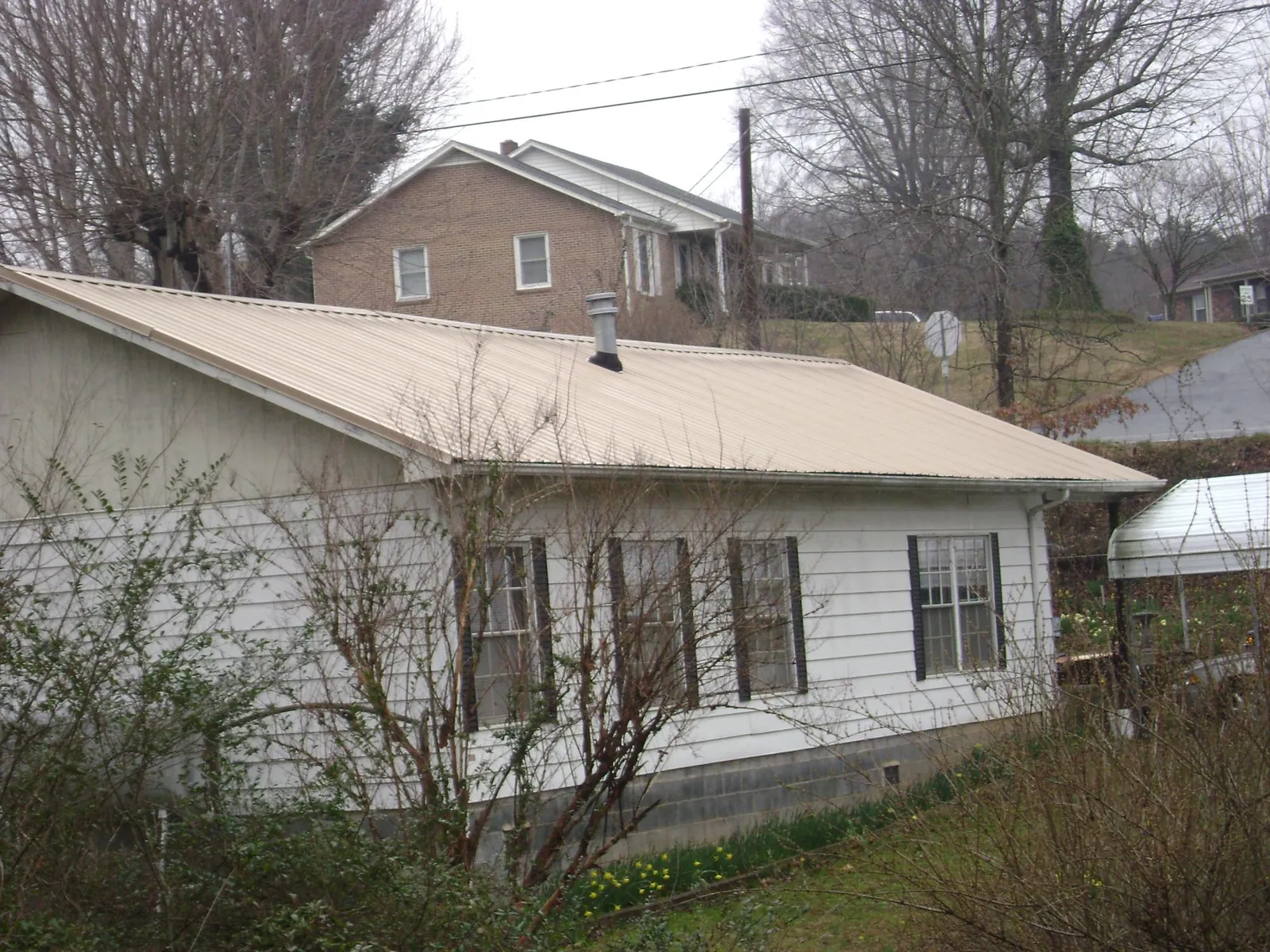 Tan metal roof on a white sided house set into a hillside — Commercial Roofing by Roofing Brothers in Mount Olivet